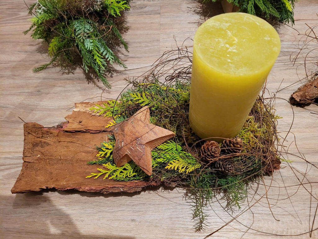 Gesteck mit Kerze, Moos und Stern auf Baumrinde
